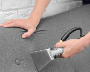Dry cleaning worker removing dirt from sofa indoors